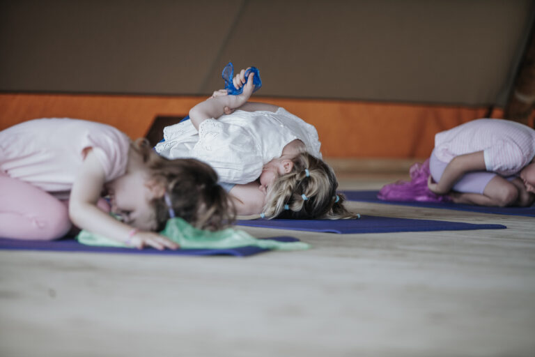 Children resting in child's pose on yoga mats with coloured scarves