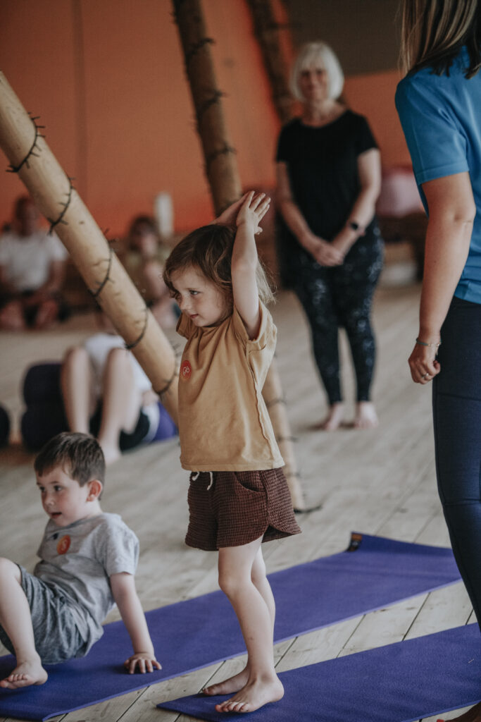Young girl balancing in a yoga pose with her teacher beside her