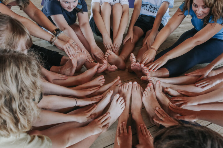 Children and a teacher sitting in a circle with their toes touching