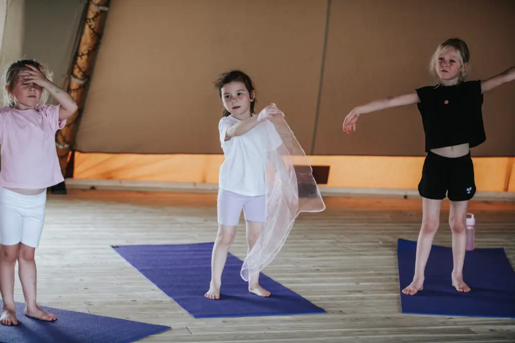 Three children standing on yoga mats with arms outstretched during a Happy Kids Yoga class