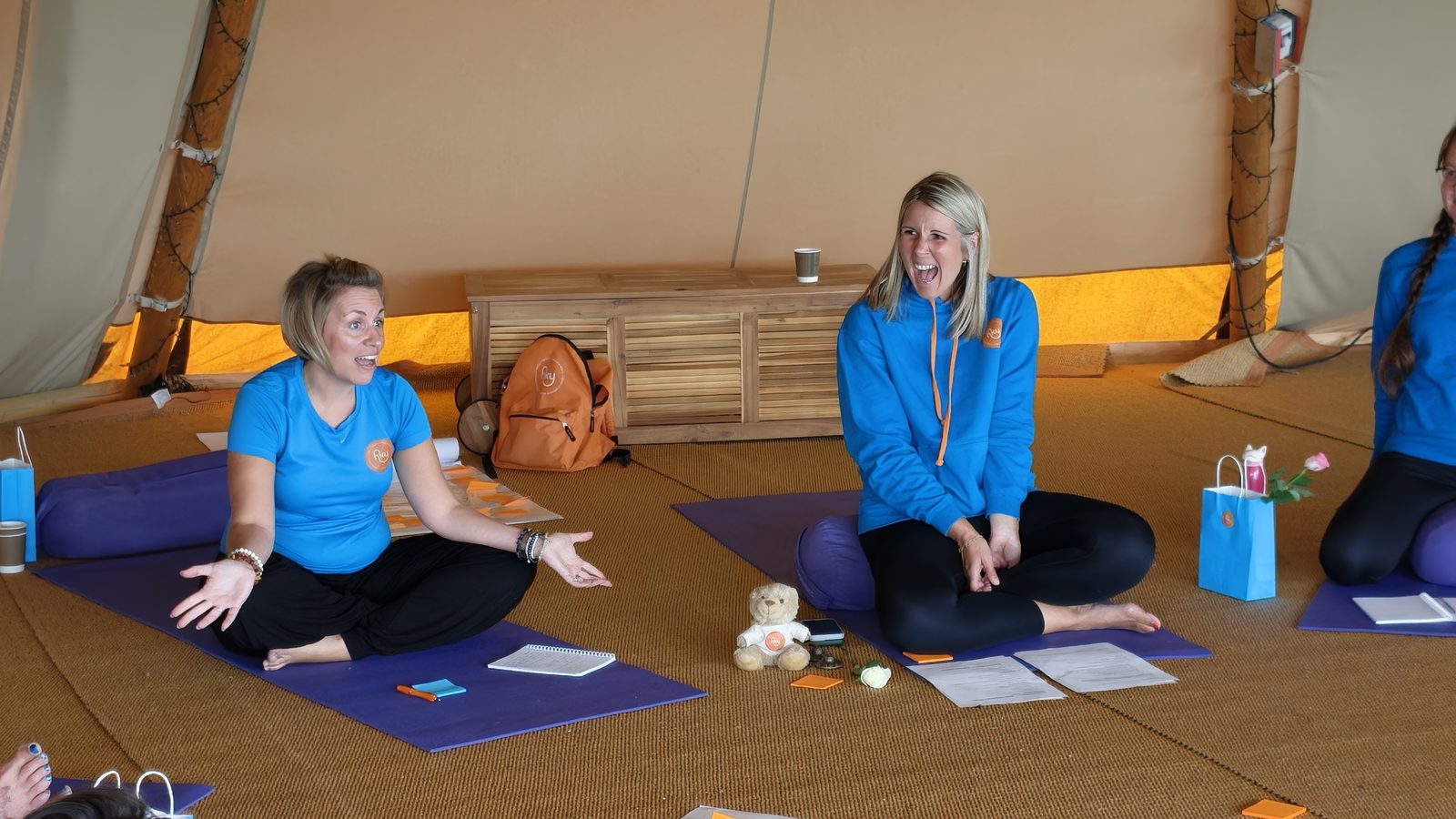 Two Happy Kids Yoga franchisees laughing together during a session at the Big Team Get Together