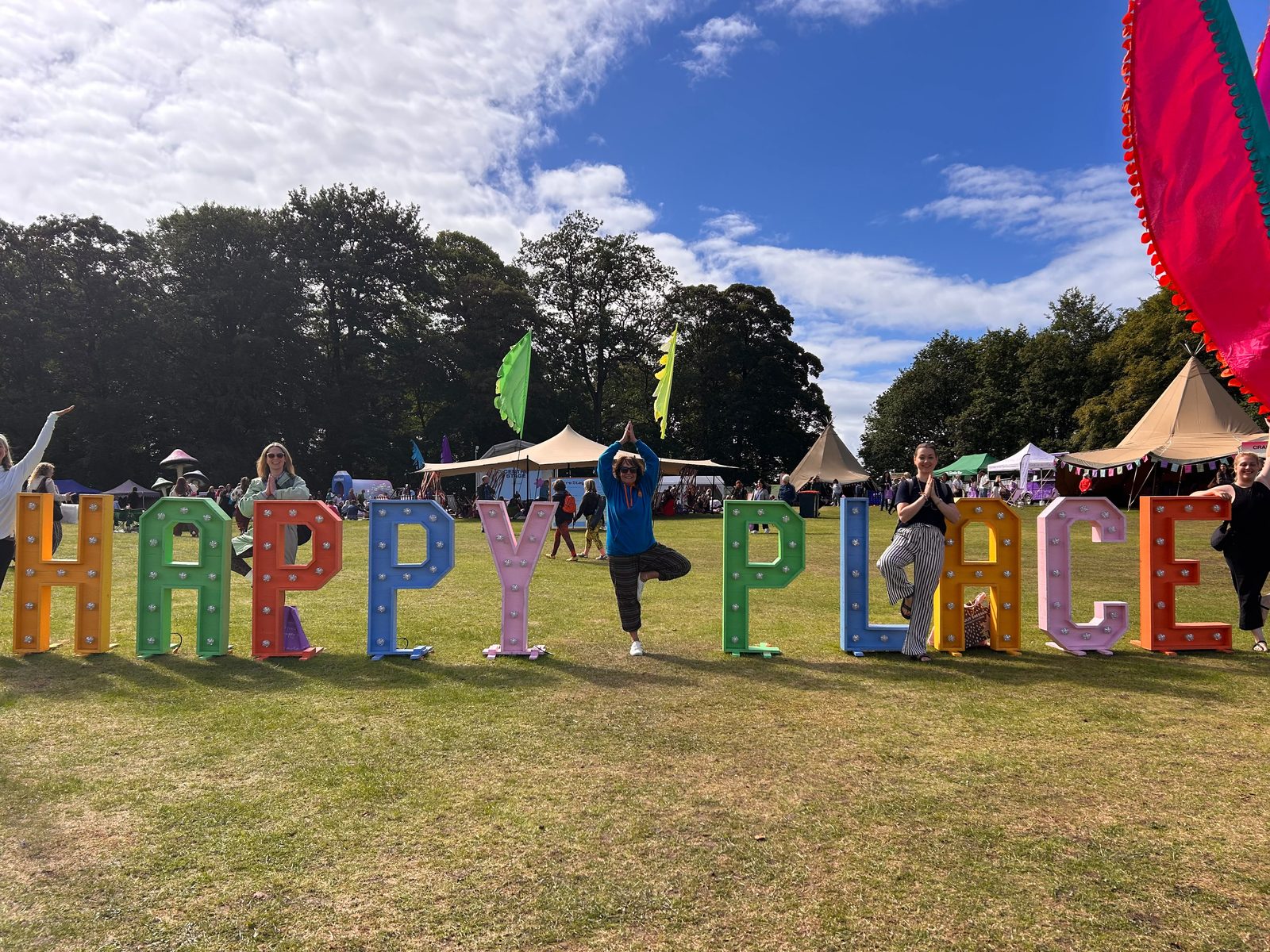 Happy Kids Yoga franchisees in tree pose beside the Happy Place Festival letters