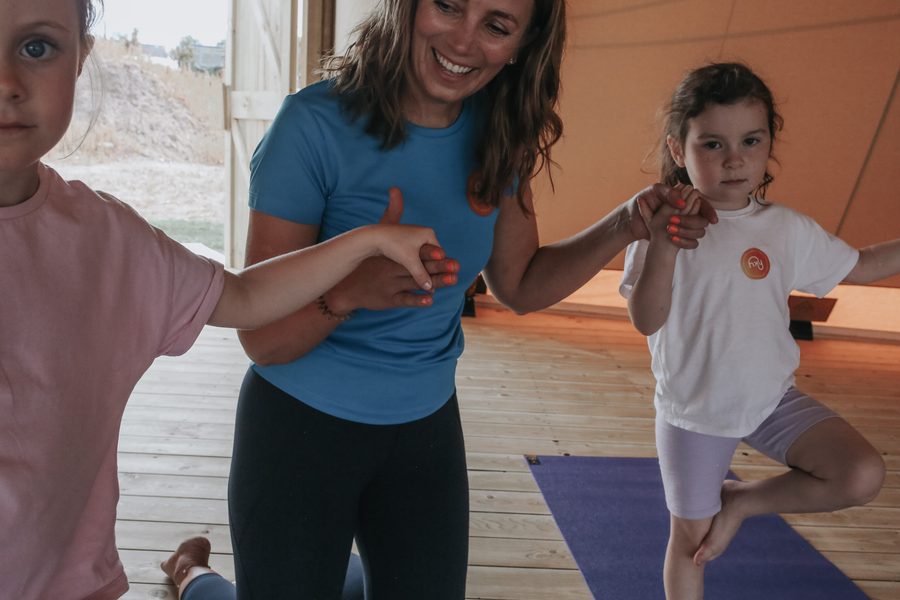 A Happy Kids Yoga teacher helping two young children balance in tree pose
