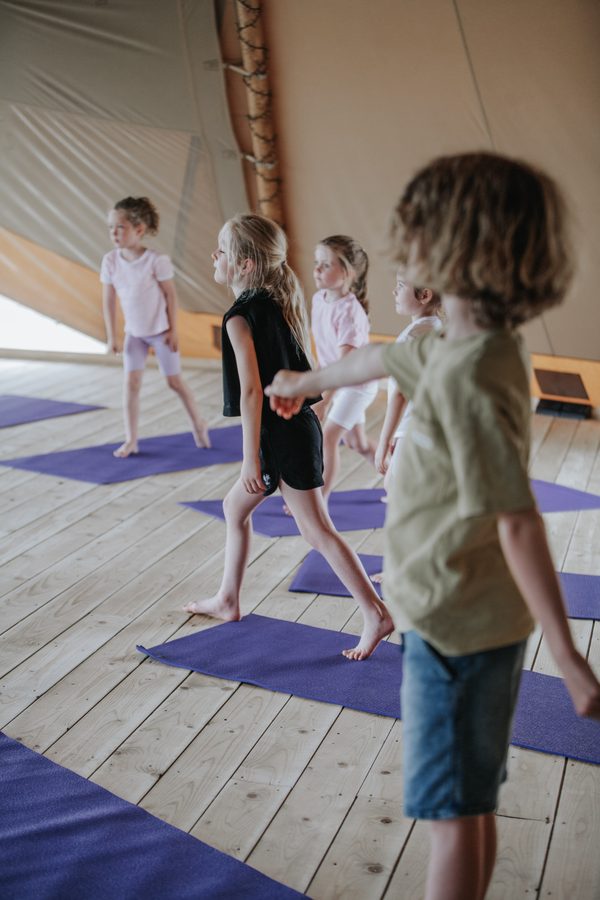 Children in a line holding a standing yoga pose