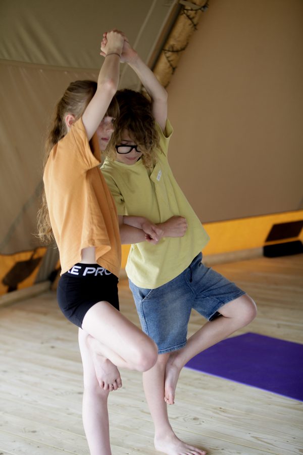Two children balancing together in a partner tree pose
