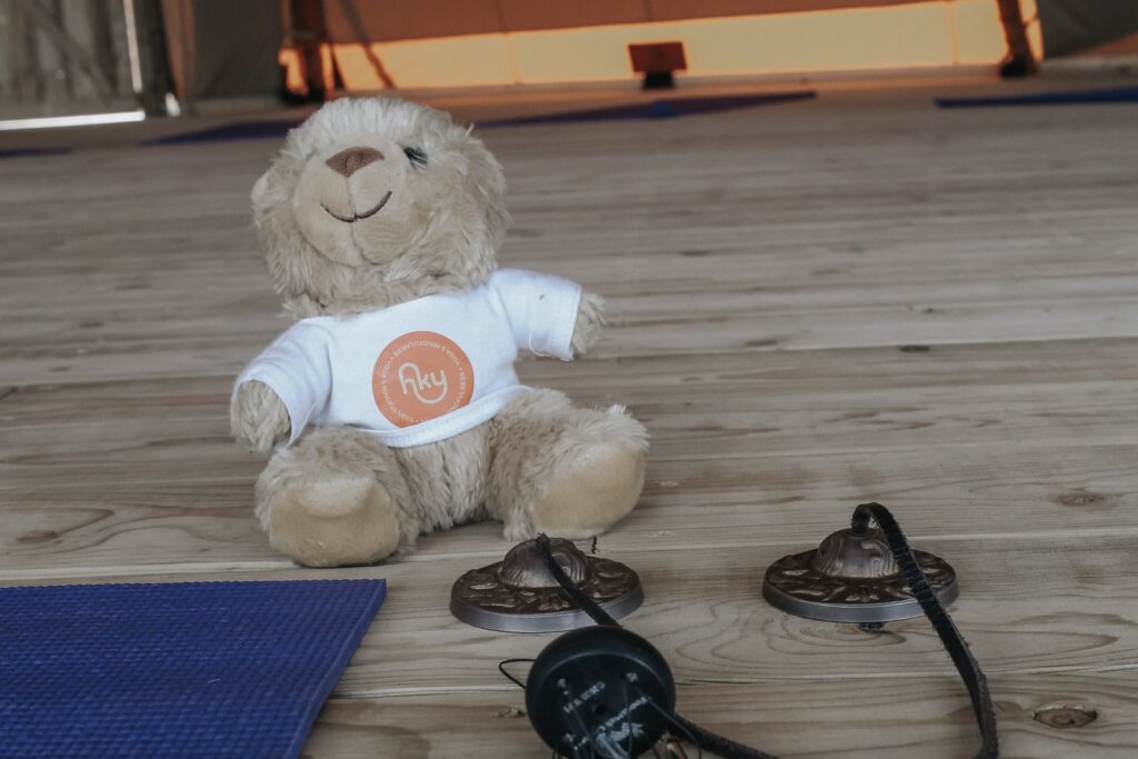 Tingsha chimes and the Happy Kids Yoga teddy beside a yoga mat